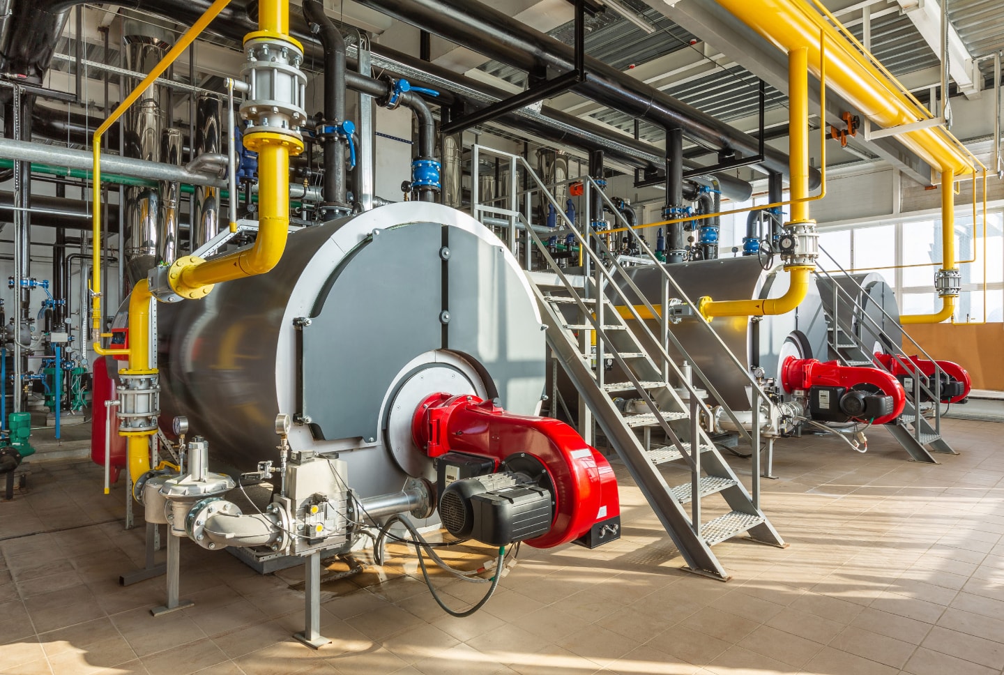 The interior of an industrial boiler room with three large boilers, many pipes, valves and sensors.
